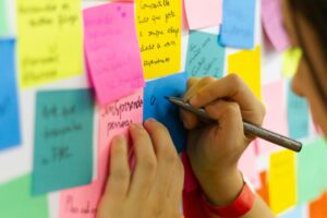 person writing on pink sticky notes