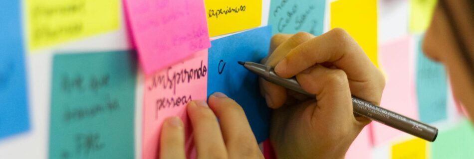 person writing on pink sticky notes